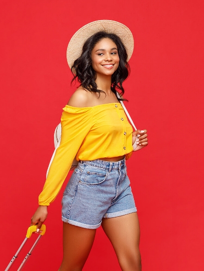 Women standing dragging a suitcase wearing a yellow shirt and hat