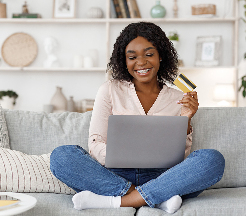 Women sitting on a couch looking at a laptop holding a credit card
