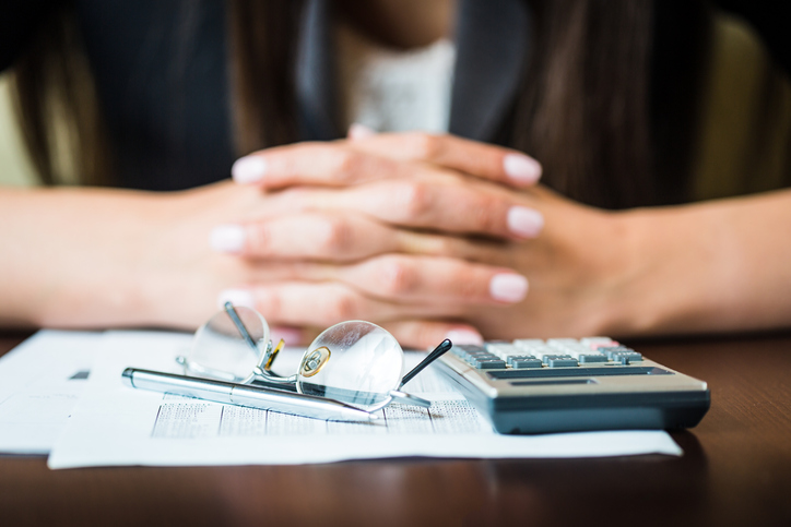 Close up of businesswomans hands with pen, glasses, and calculator doing some financial calculations