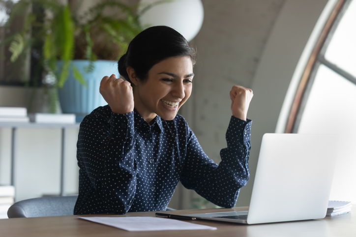 young woman with fists in the air, excitedly looking at her laptop