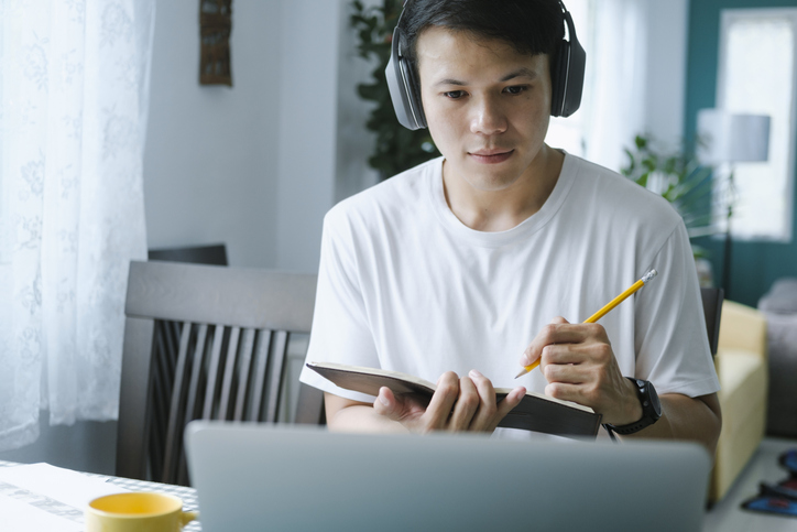 young man studying laptop while taking notes