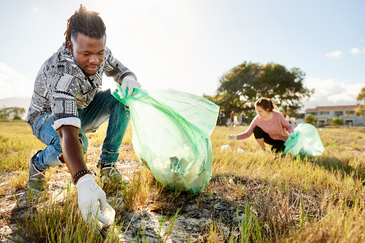 Two young volunteers picking up litter and putting it in bags during a community cleanup day in a field