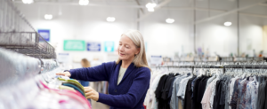 woman smiling searching for shirts in a clothing rack at Goodwill