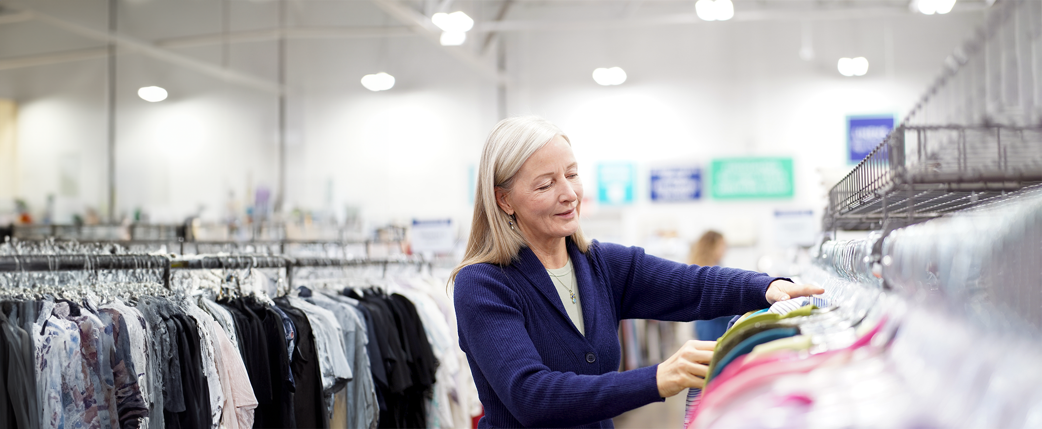 woman smiling searching for shirts in a clothing rack at Goodwill